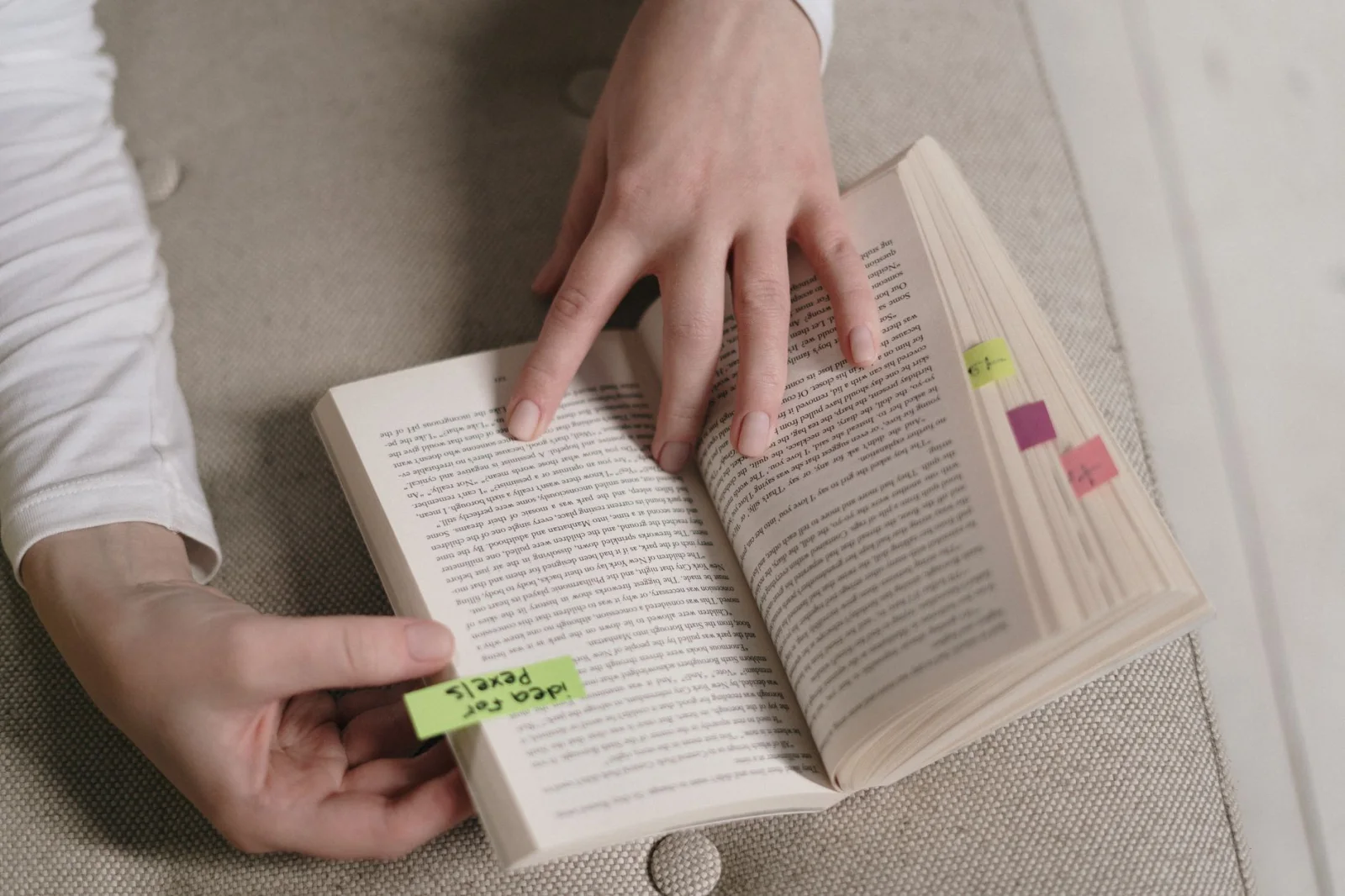 Uma pessoa segura um livro aberto com várias abas adesivas coloridas enquanto folheia uma página, vista de perto.