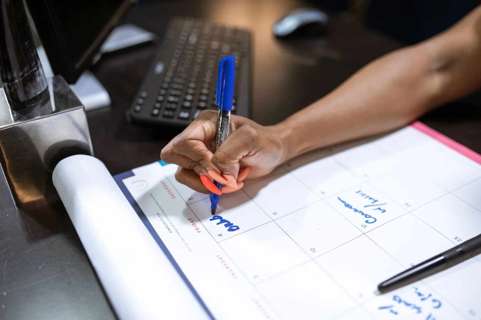 Close-up of a person's hand writing notes on a calendar using a blue marker.