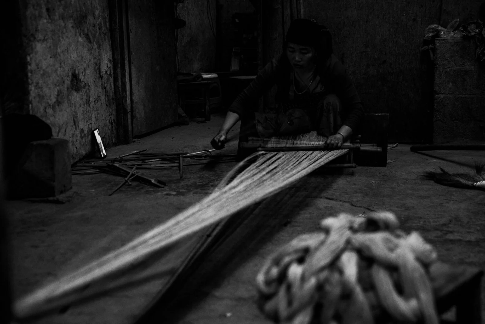Woman attentively weaving fabric in a traditional artisan setting, in black and white.