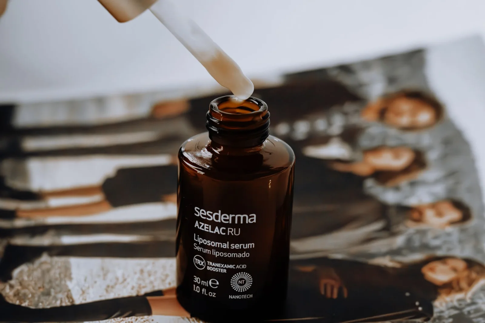 Sesderma Azelac RU liposomales Serumfläschchen mit Pipette auf einem unscharfen Magazin im Hintergrund.
