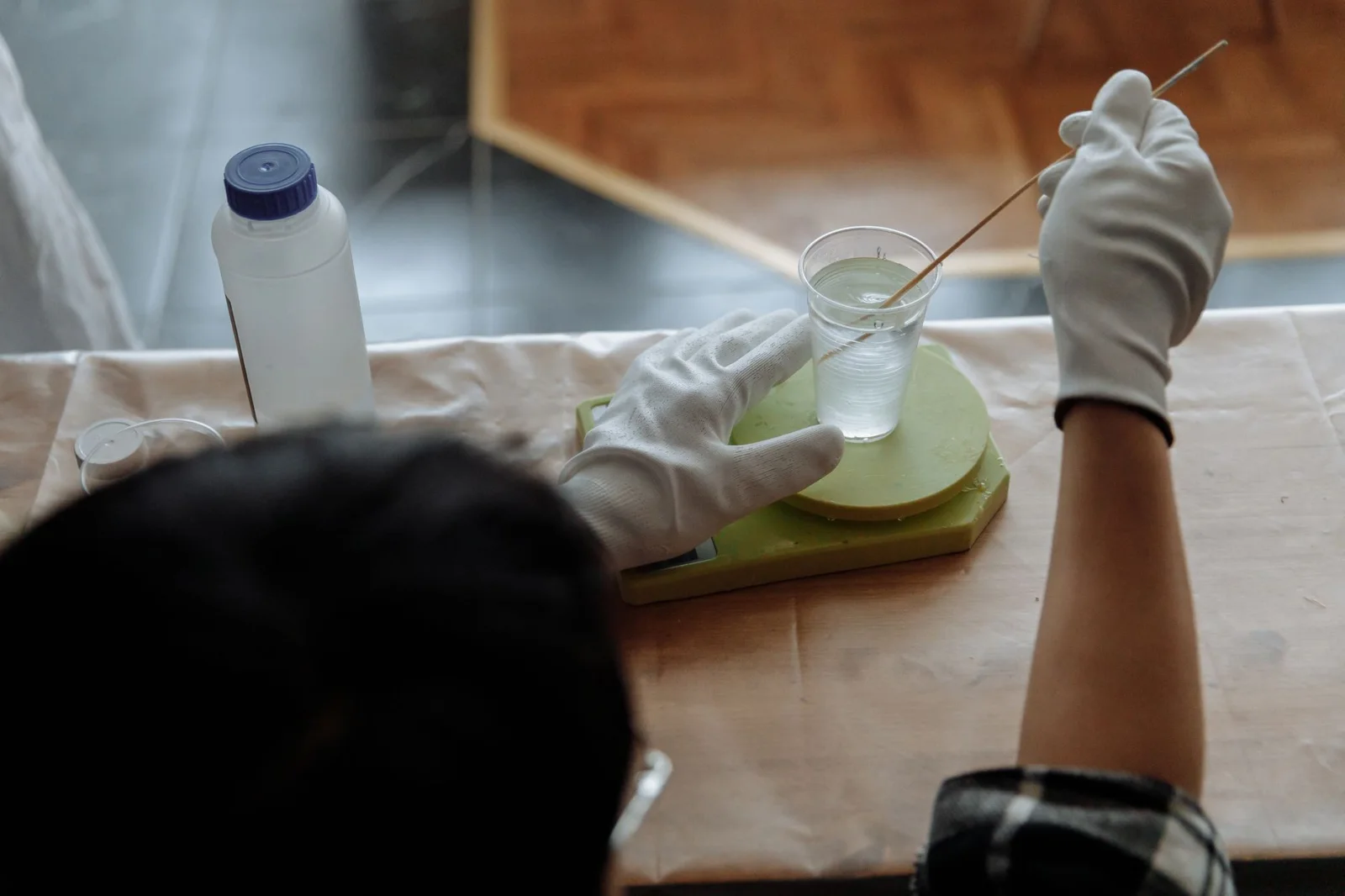 Halbnahaufnahme eines Mannes mit Handschuhen, der im Werkstattumfeld transparentes Harz in einem Plastikbecher mischt.