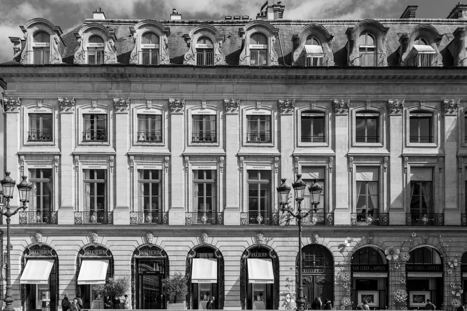 Fotografia in bianco e nero della facciata di un edificio parigino vintage con dettagli architettonici e diverse finestre con tende da sole.