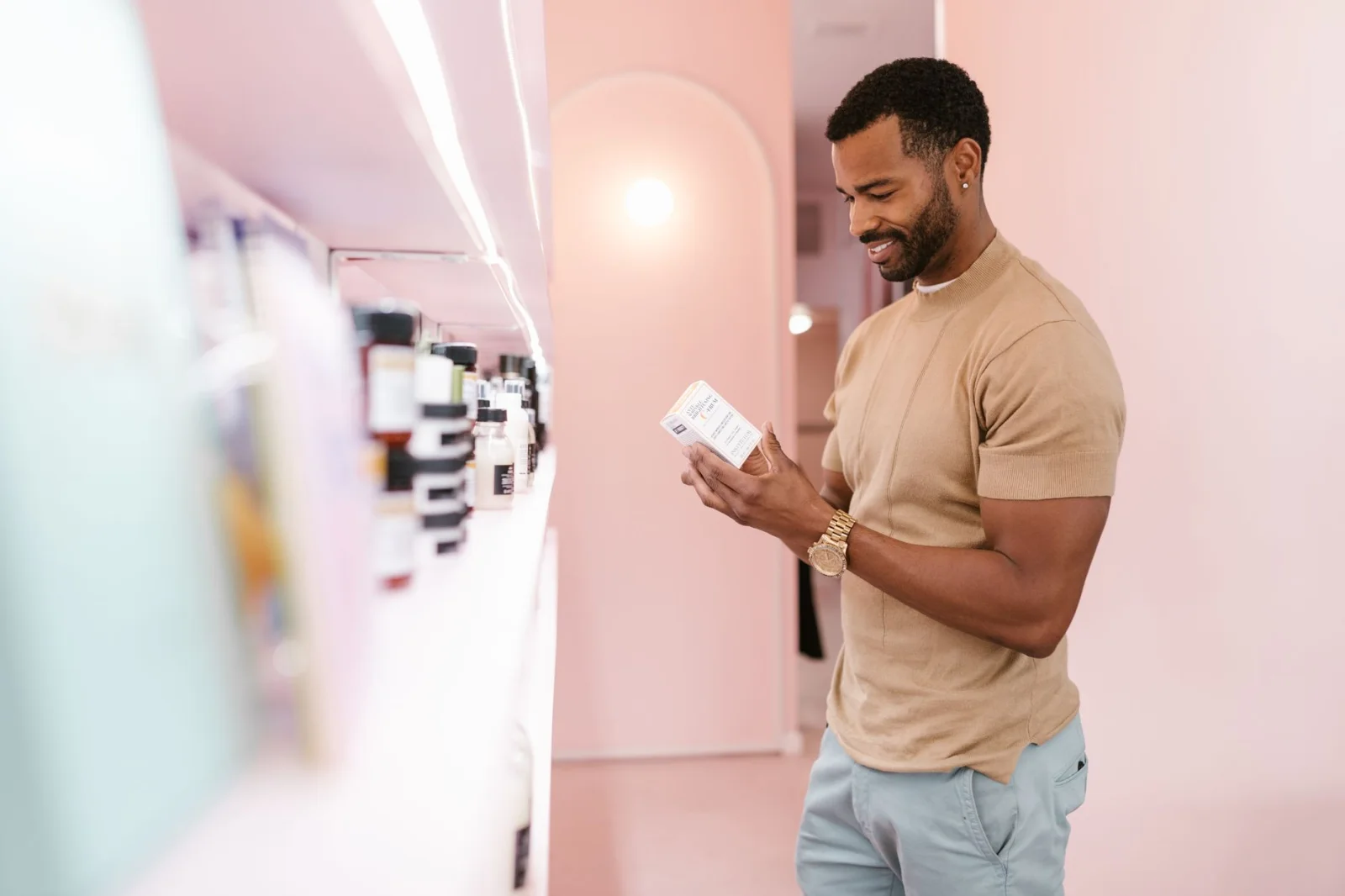 Hombre examina la etiqueta de un producto para el cuidado de la piel en una tienda moderna y bien iluminada.