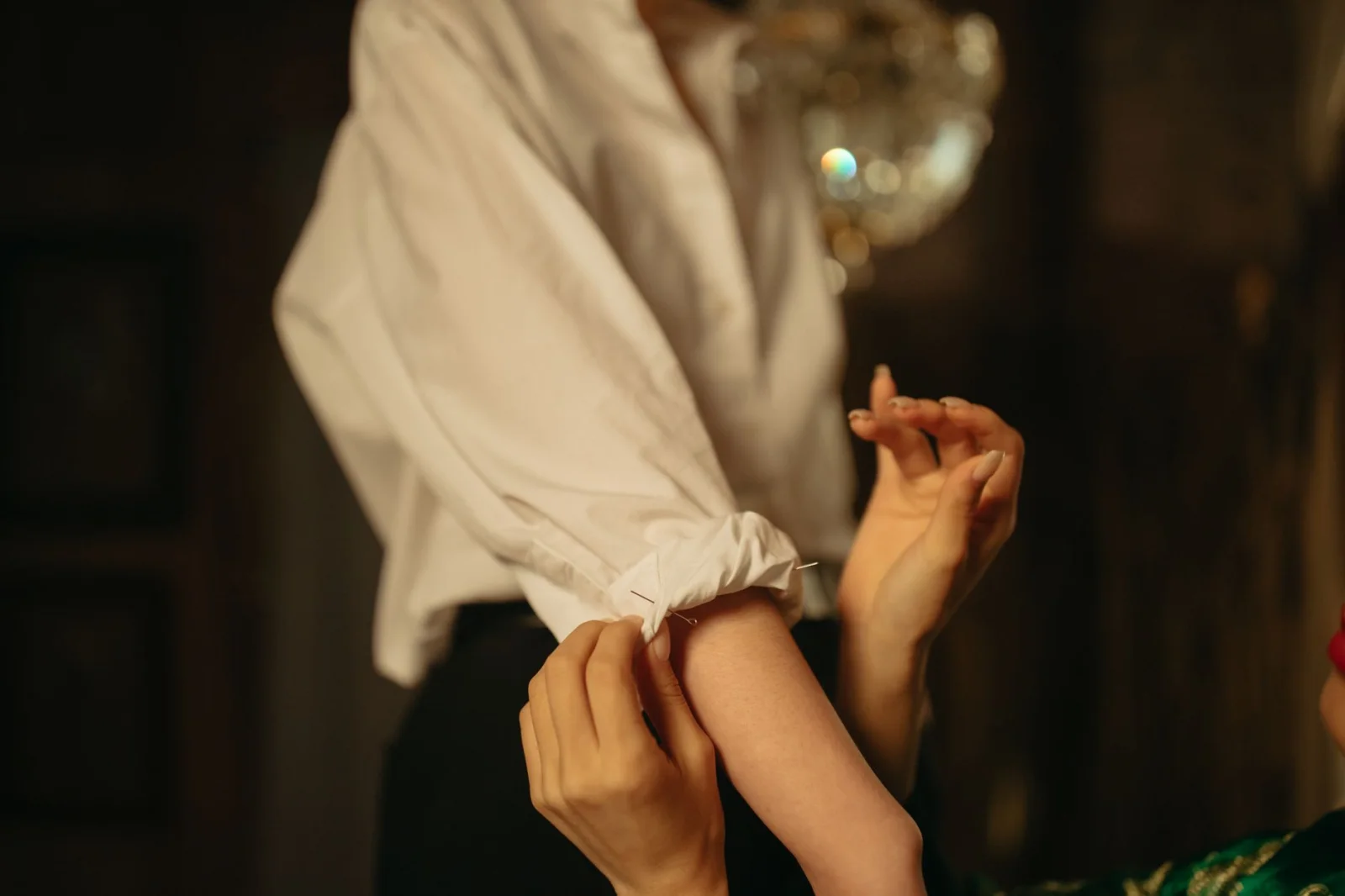 Close-up of a person adjusting the sleeve of a white shirt, highlighting the garment and tailoring details.