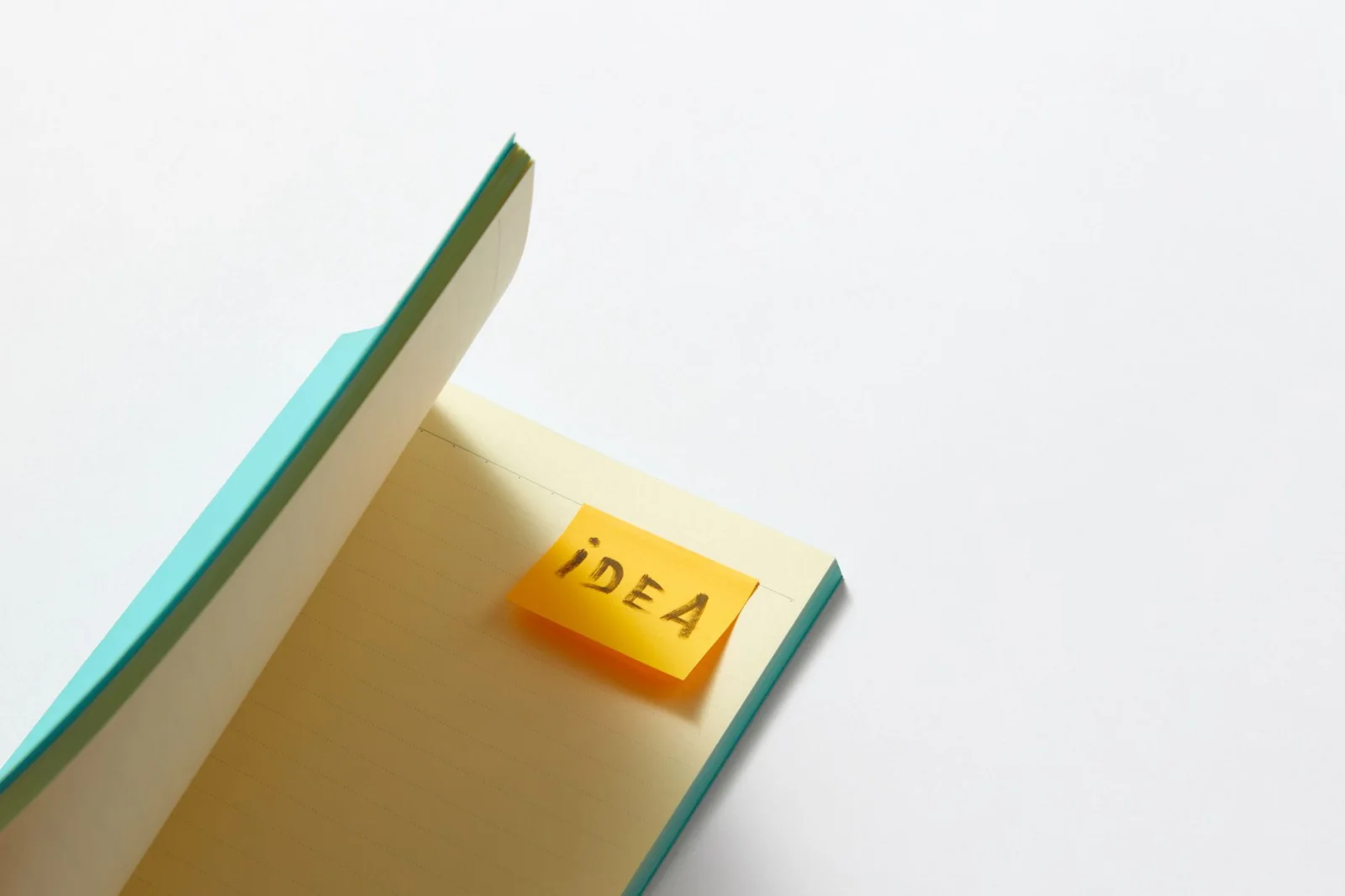 Quaderno aperto con un post-it giallo con la scritta 'idea' su una superficie bianca.