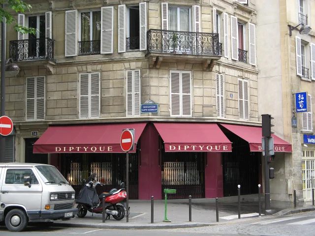 Exterior of the Diptyque store on Boulevard Saint Germain in Paris featuring red awnings and white shuttered windows.