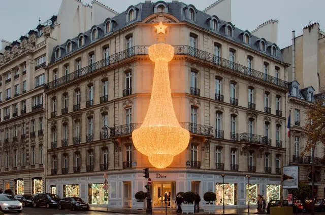 Konzeptbild des Dior-Geschäfts in der 30 Avenue Montaigne in Paris, Frankreich, mit beleuchteten Dekorationen in Form eines Sterns und großem Kronleuchter an der Fassade des historischen Gebäudes.