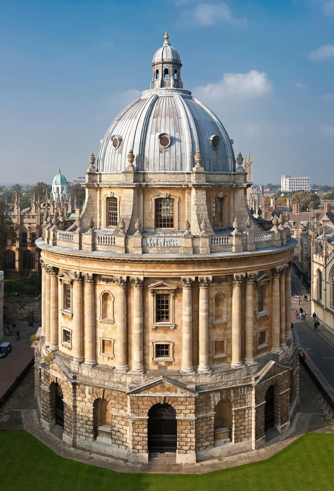 Fotografie des Radcliffe-Camera-Gebäudes in Oxford, England, mit seiner markanten Kuppel und klassischer Architektur über grünem Rasen unter klarem blauem Himmel.