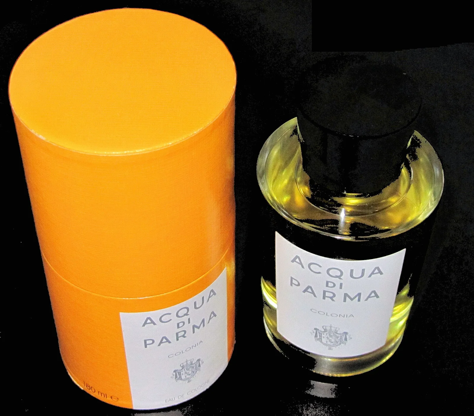 Konzeptbild zeigt eine Flasche Acqua di Parma Colonia Eau de Cologne neben der charakteristischen gelben zylindrischen Verpackung vor schwarzem Hintergrund.