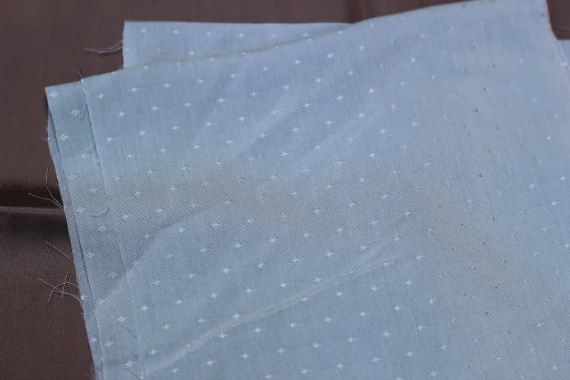 Tissu dobby bleu doux avec un motif géométrique répété de petits losanges, posé sur une surface marron.